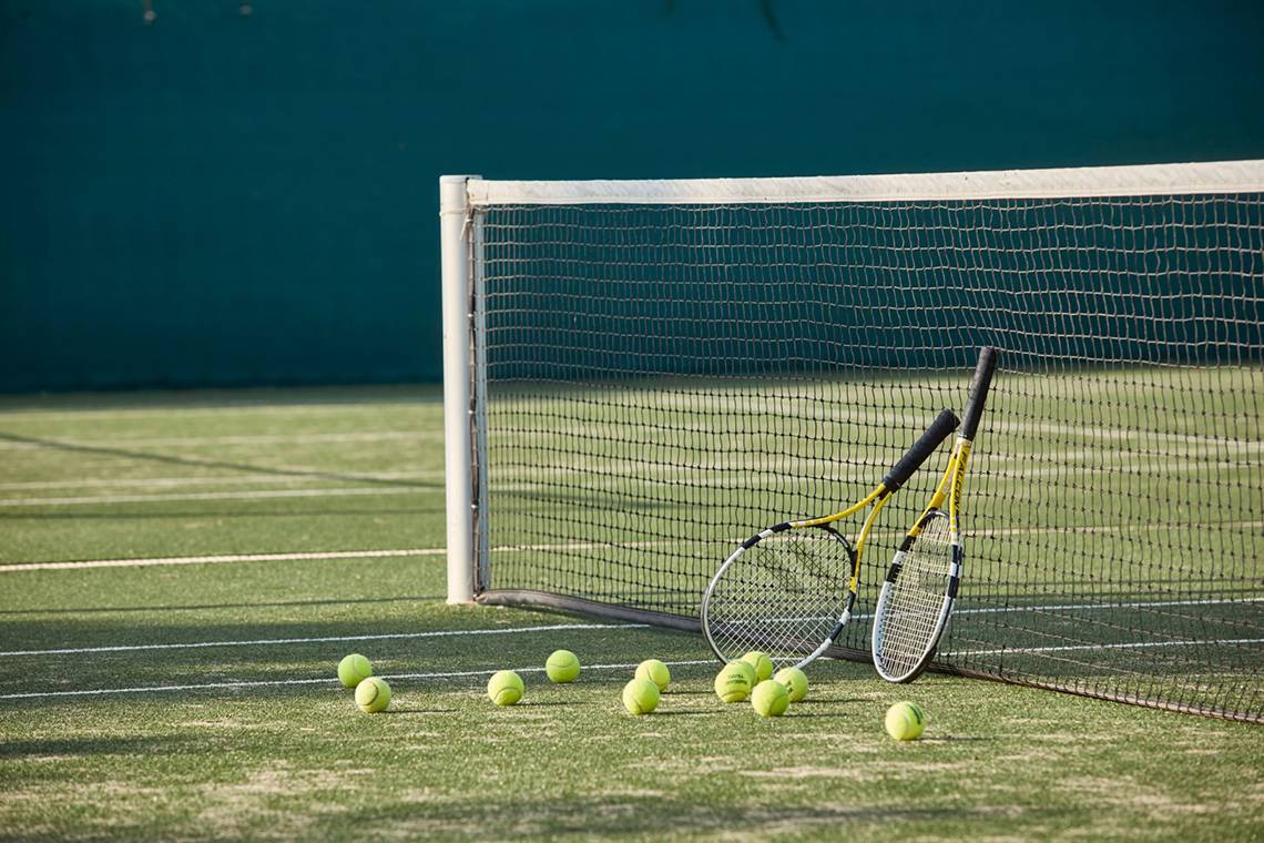 Tennisschläger und Bälle liegen auf einem Tennisplatz neben einem Netz.