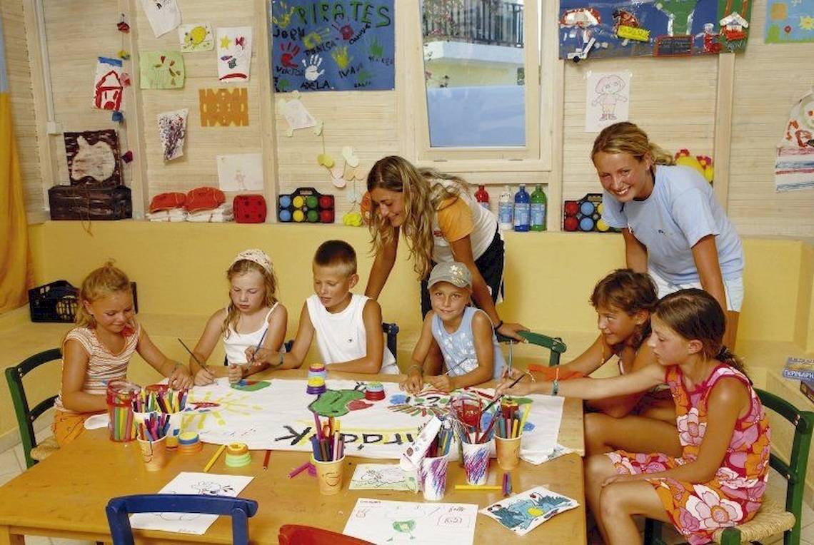 Gruppe von Kindern malt an einem Tisch im Cactus Village Hotel, während zwei Frauen helfen.