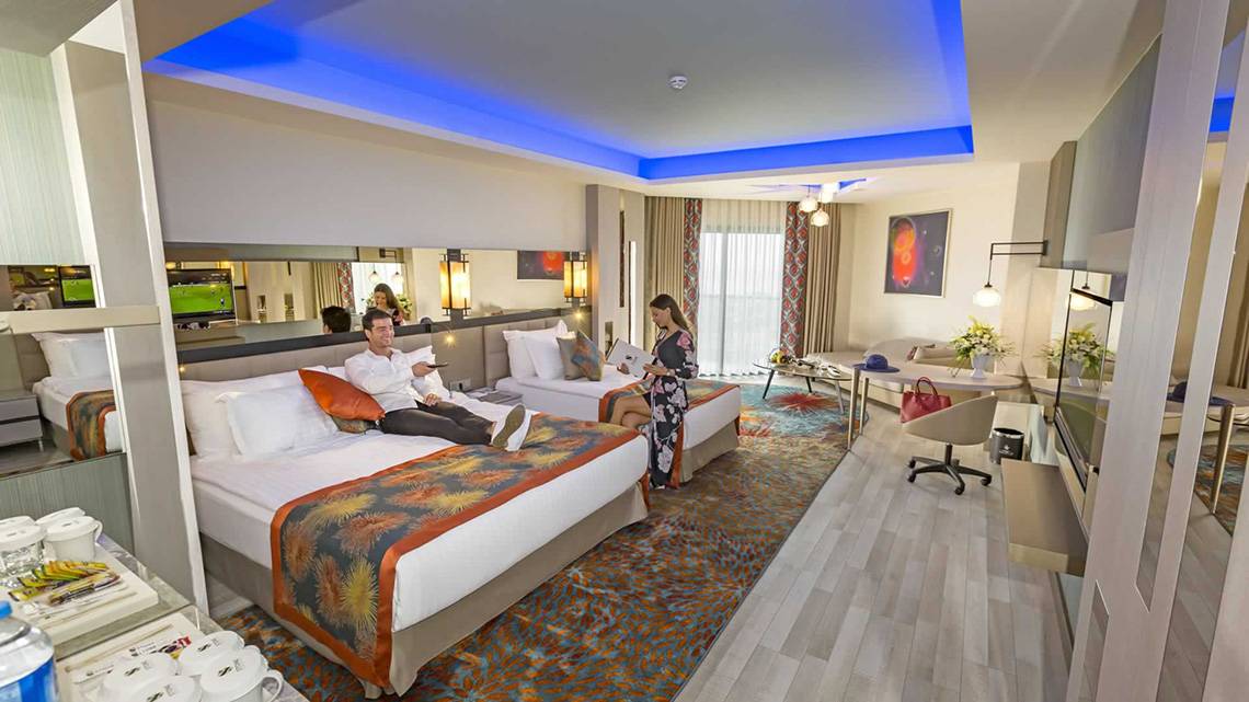 Zwei Betten in einem eleganten Hotelzimmer von Royal Seginus mit einer Frau, die liest, und einem Mann, der entspannt.