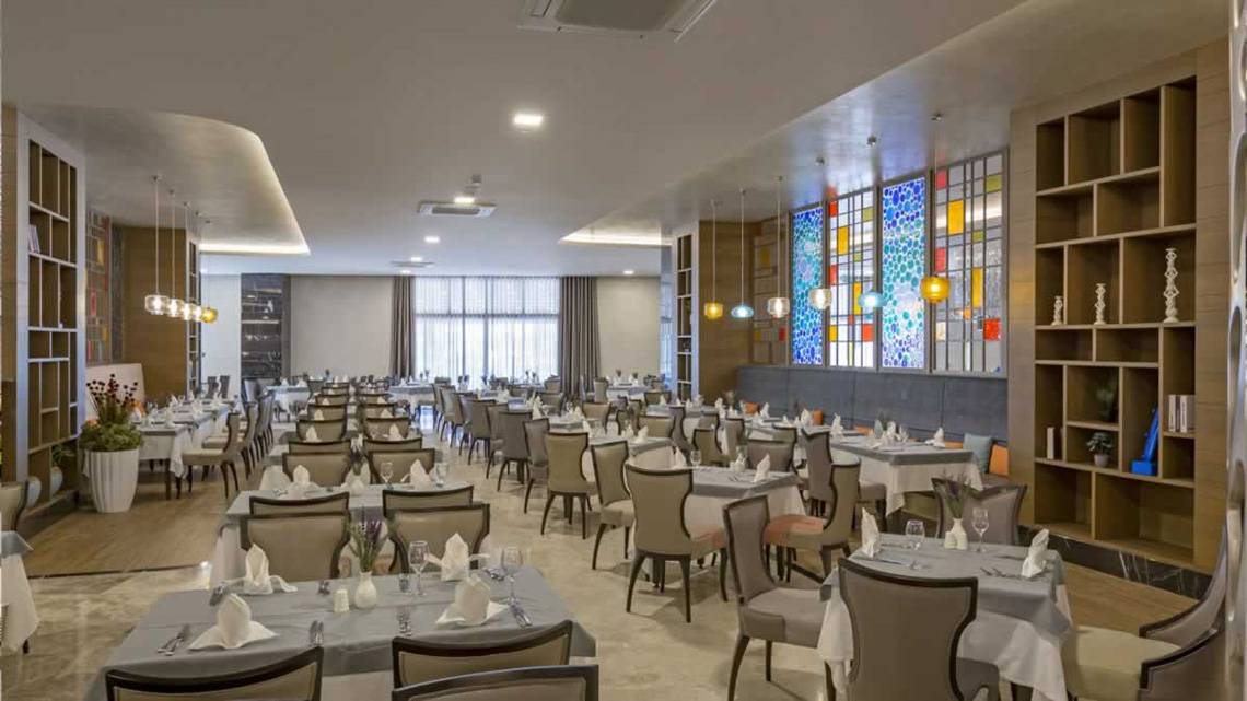 Das elegante Restaurant des Royal Seginus Hotels mit vielen Tischen und Stühlen, bunten Glasfenstern und Holzregalen.