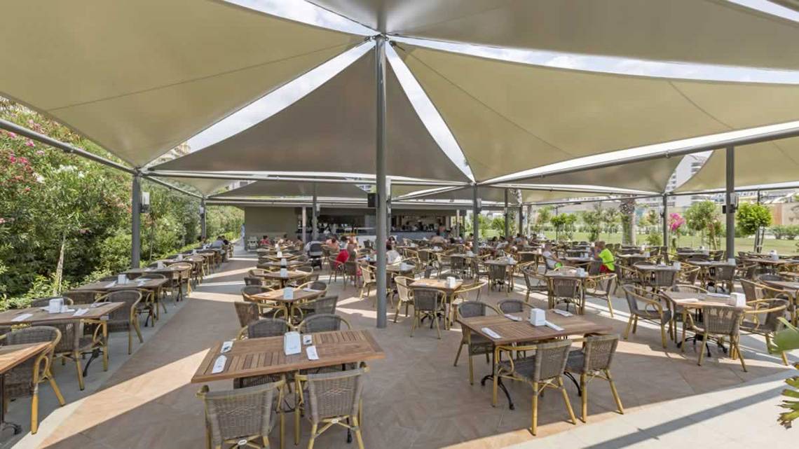 Outdoor-Restaurant im Royal Seginus Hotel mit vielen Gästen unter Sonnensegeln.