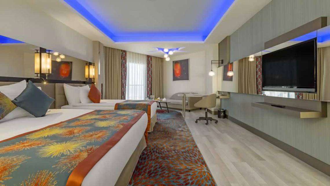 Innenansicht eines Zimmers im Royal Seginus Hotel mit zwei Betten, einem Schreibtisch und einem Fernseher.
