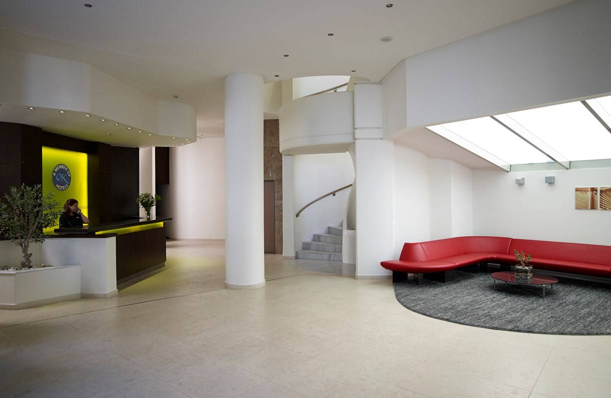 Empfangsbereich des Kriti Beach Hotel mit Rezeption, roten Sofas und zentraler Treppe.