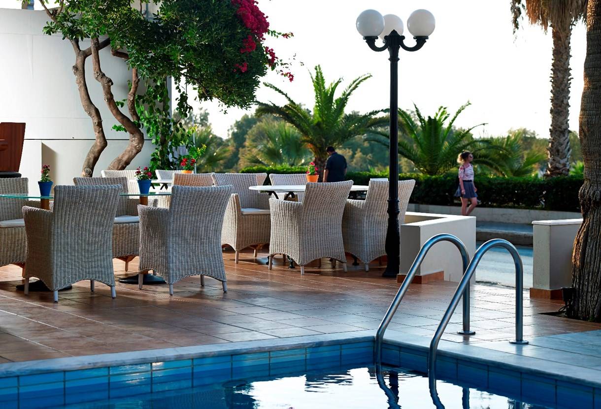 Terrasse des Kriti Beach Hotels mit Tischen, Stühlen und Swimmingpool.