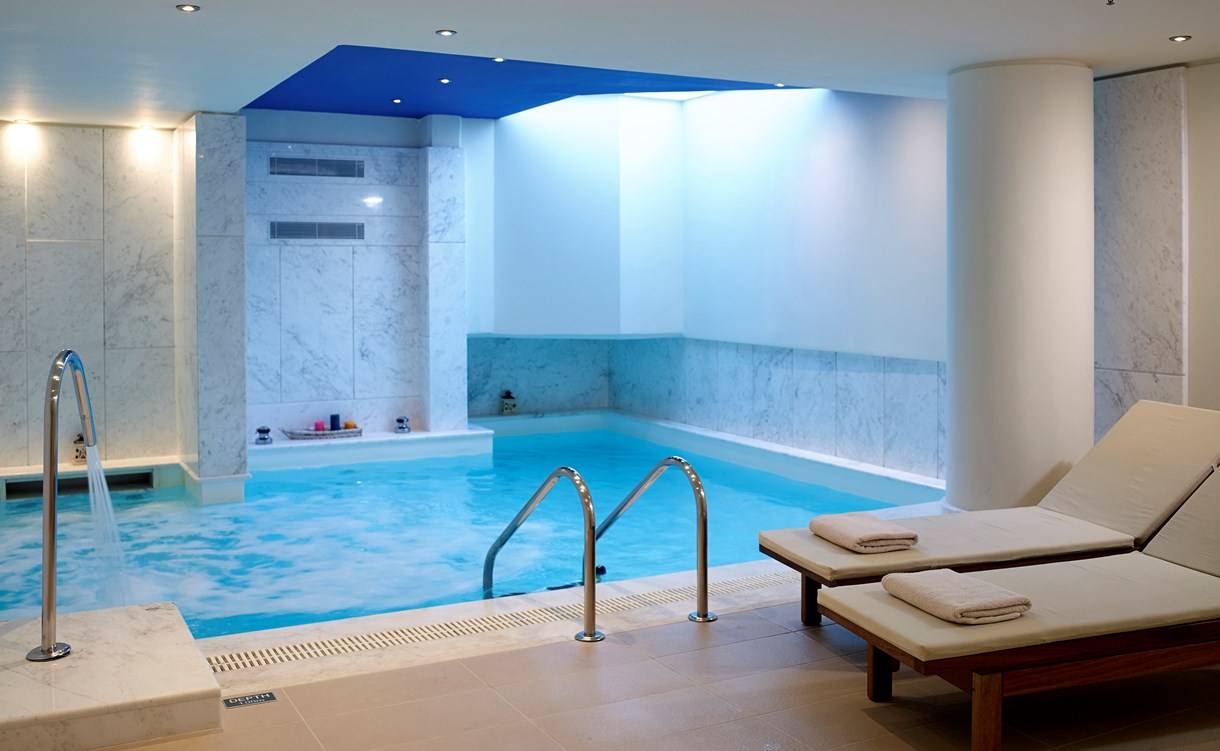 Innenpool im Kriti Beach Hotel mit weißen Marmorwänden und zwei Liegestühlen