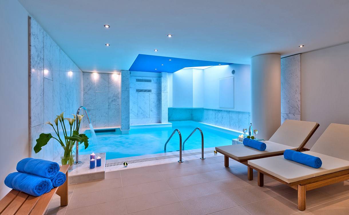 Innenpool-Bereich im Kriti Beach Hotel mit Lounge-Liegestühlen und blauen Handtüchern.