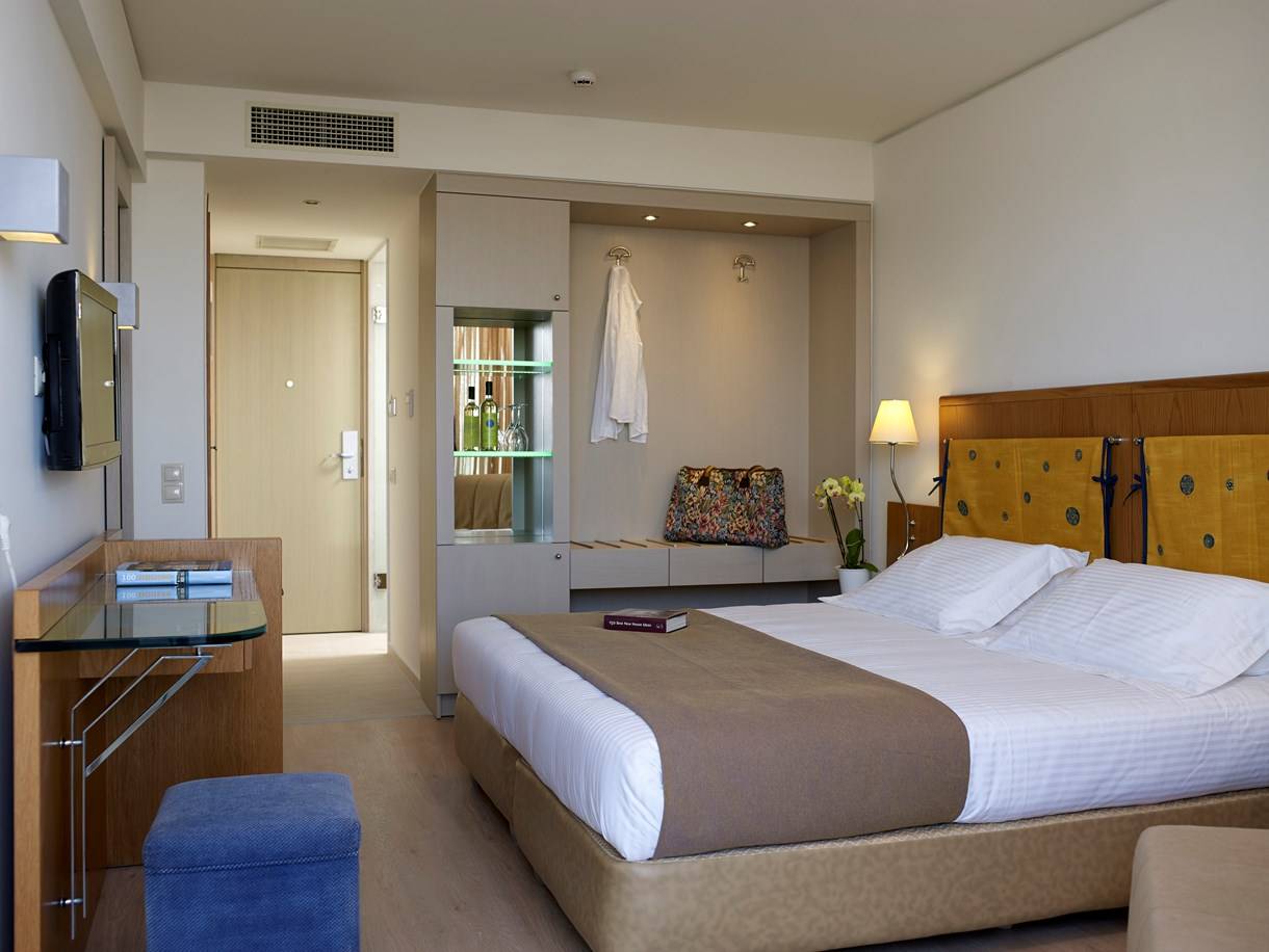 Ein elegantes Hotelzimmer im Kriti Beach Hotel mit einem großen Bett und einem Schreibtisch.