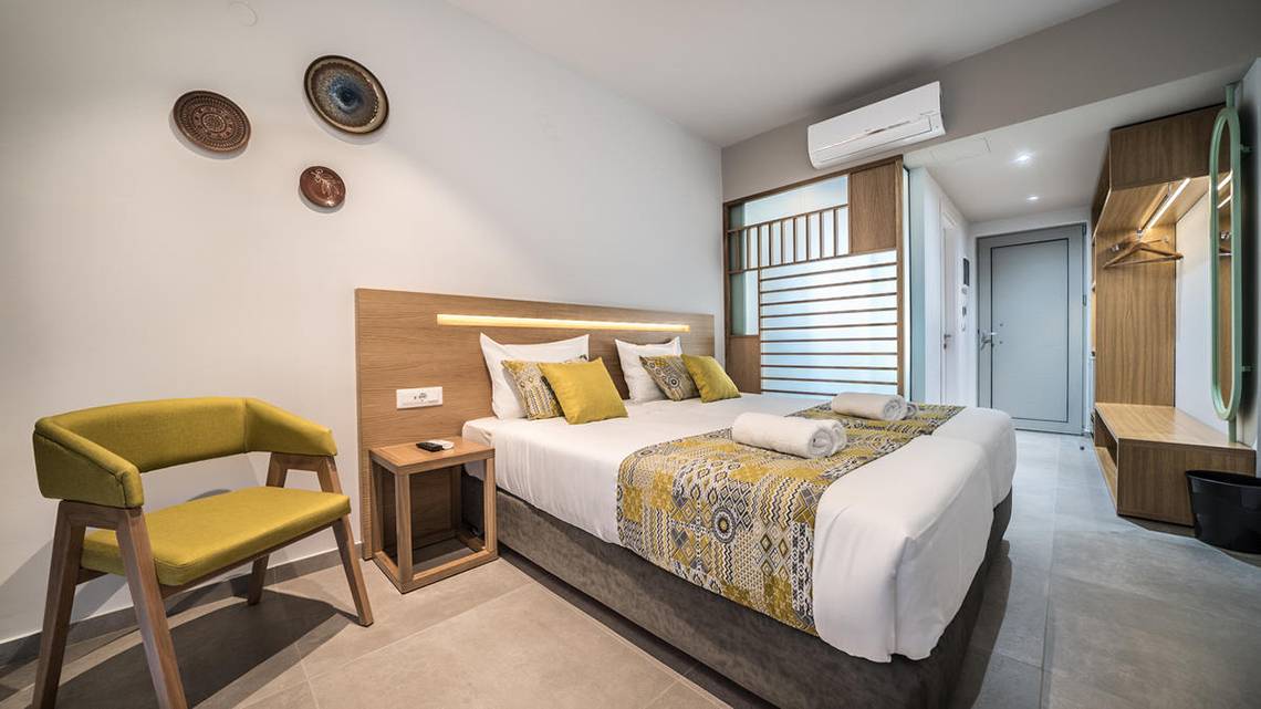 Ein elegantes Hotelzimmer im Adele Beach Hotel mit einem Bett, gelben Kissen und einem grünen Stuhl.