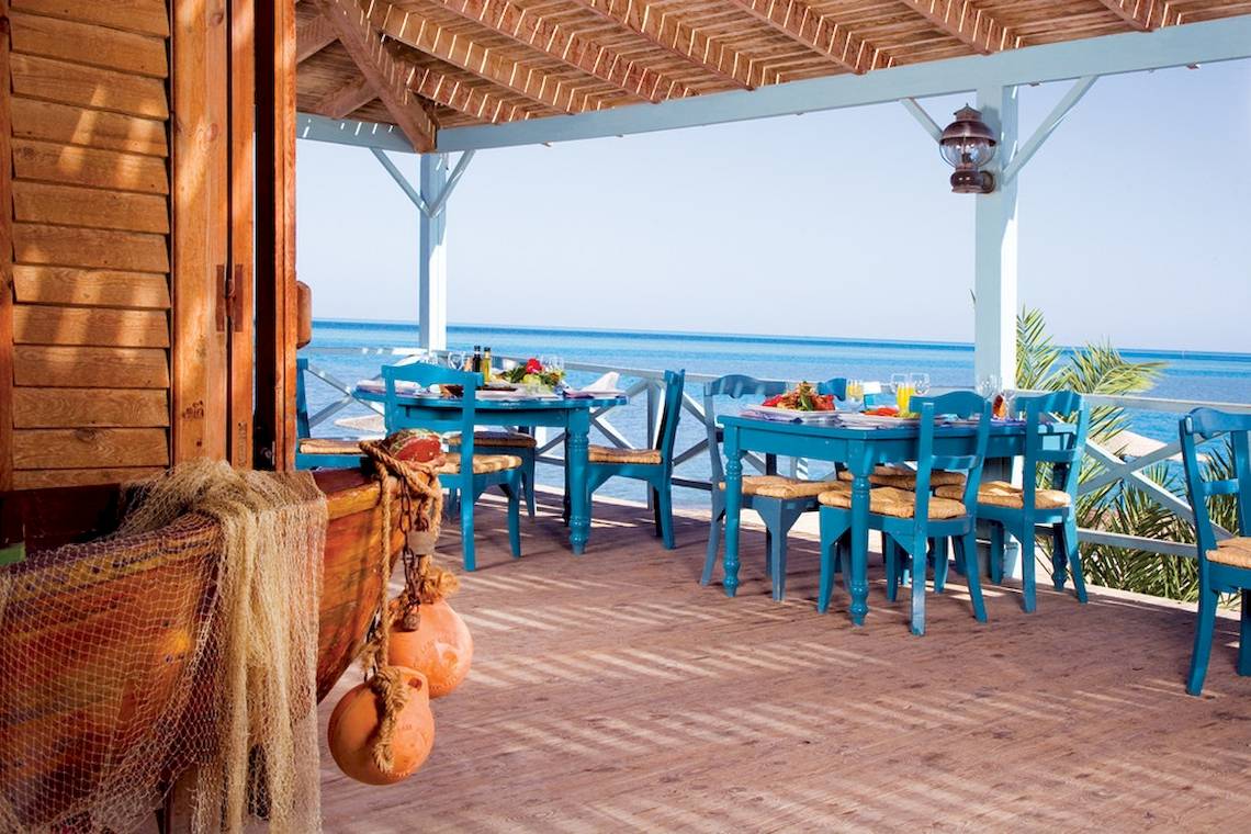 Terrasse des Mövenpick Resort & Spa El Gouna mit blauen Tischen und Stühlen und Blick auf das Meer.