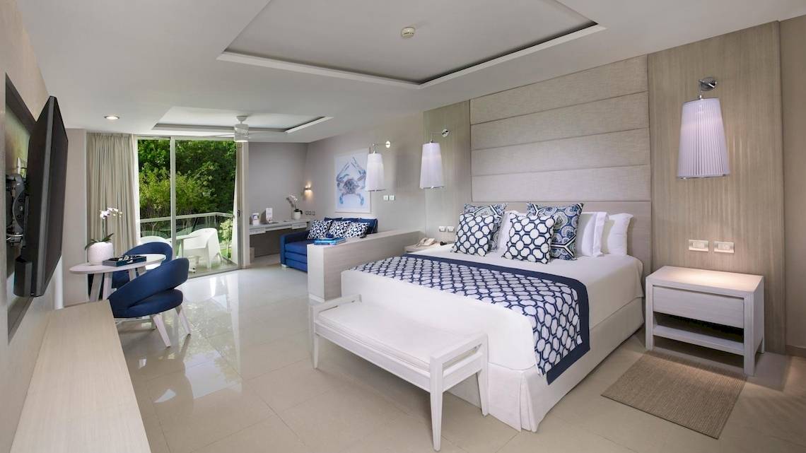 Ein elegantes Schlafzimmer im Grand Sirenis Riviera Maya Resort & Spa mit einem großen Bett, blauen Kissen und einer modernen Einrichtung.