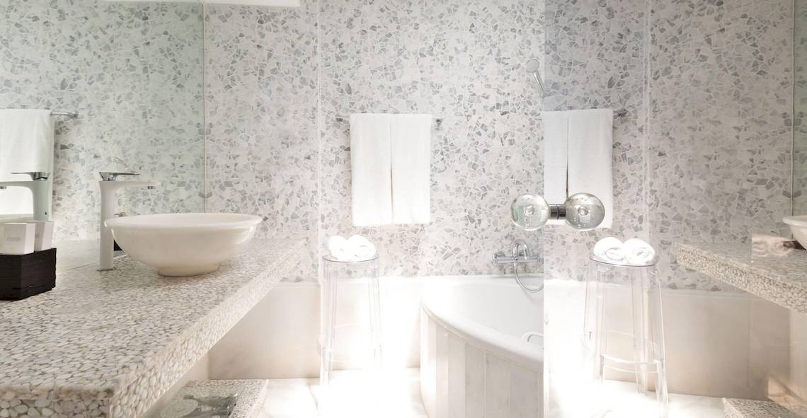 Badezimmer im Kivotos Mykonos Hotel mit mosaikartigen Wänden, weißem Waschbecken und Badewanne.