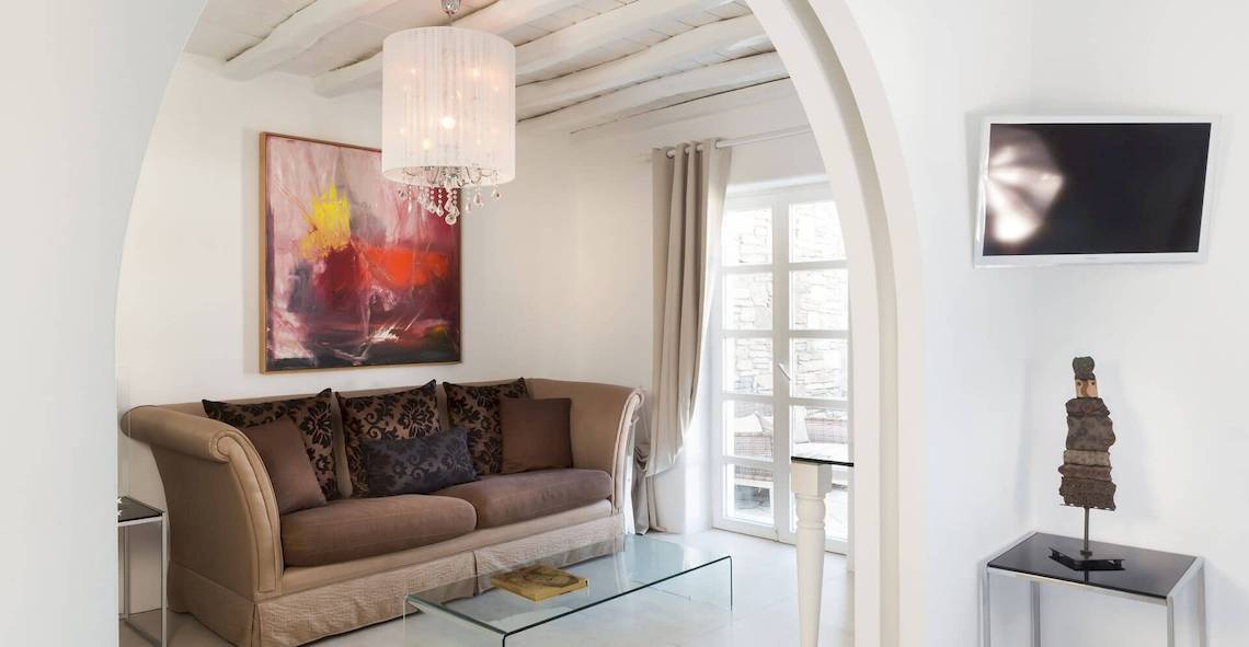 Wohnzimmer im Kivotos Mykonos Hotel mit Couch, Glastisch, Gemälde, Fernseher und Dekor.