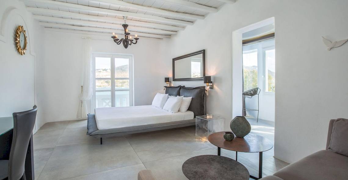 Innenansicht eines Zimmers im Kivotos Mykonos Hotel mit weißem Bett, Dekor und Möbeln.