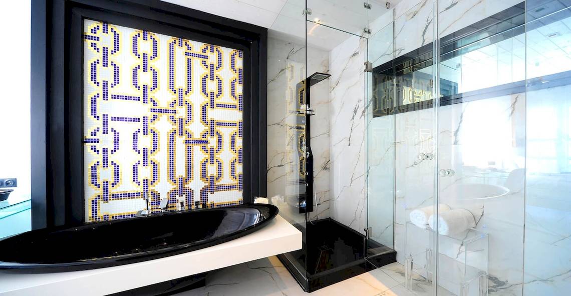 Innenansicht eines Badezimmers im Kivotos Mykonos Hotel mit schwarzer Badewanne und gefliester Wand.