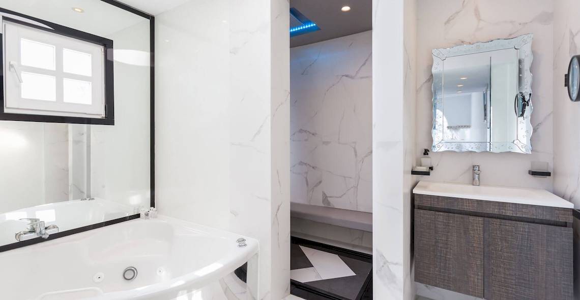 Das Badezimmer von Kivotos Mykonos mit einer Badewanne, einer Dusche, einem Spiegel und einem Waschbecken.