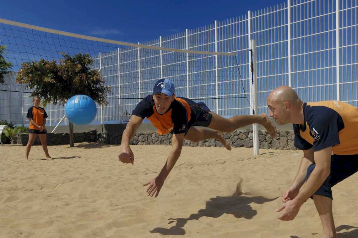 Zwei Männer spielen Volleyball am Strand mit einem blauen Ball.