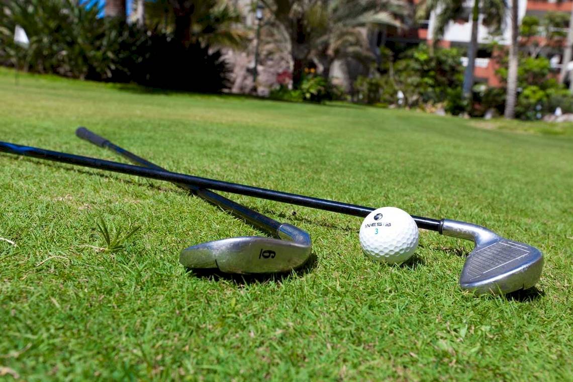 Golfschläger und Ball auf dem Rasen mit Gebäuden im Hintergrund