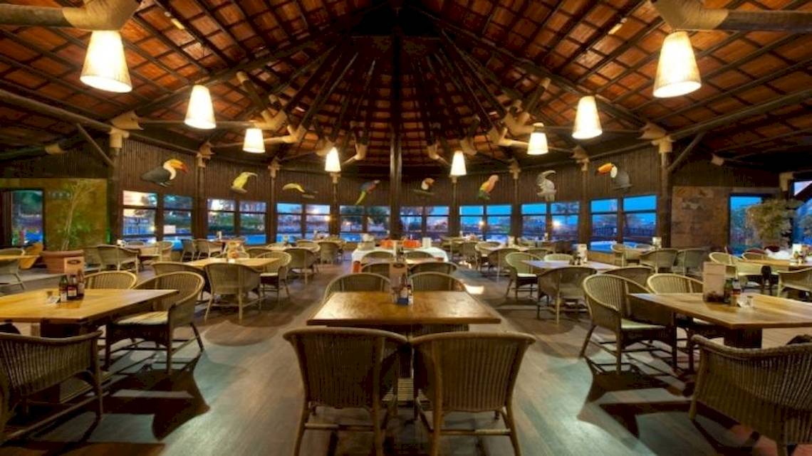 Innenbereich des Restaurants im Elba Sara Beach & Golf Resort mit Holzmöbeln und großen Fenstern.