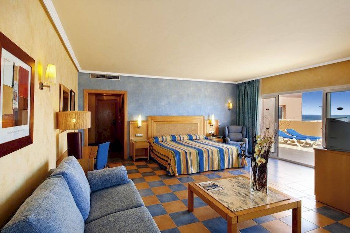 Hotelzimmer im Elba Sara Beach & Golf Resort mit Bett, Sofa, Tisch und Meerblick.