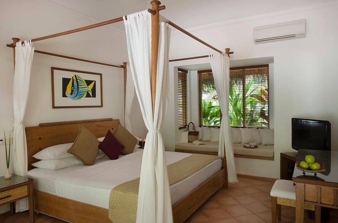 Schlafzimmer im Kuramathi Maldives Hotel mit Himmelbett, Fenstern und Klimaanlage.