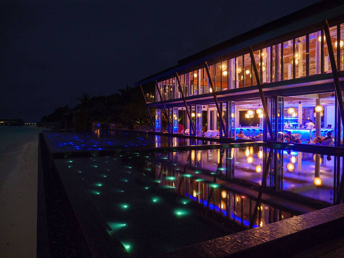 Nachtansicht des Kuramathi Maldives Hotels mit beleuchtetem Pool und Innenbereich.