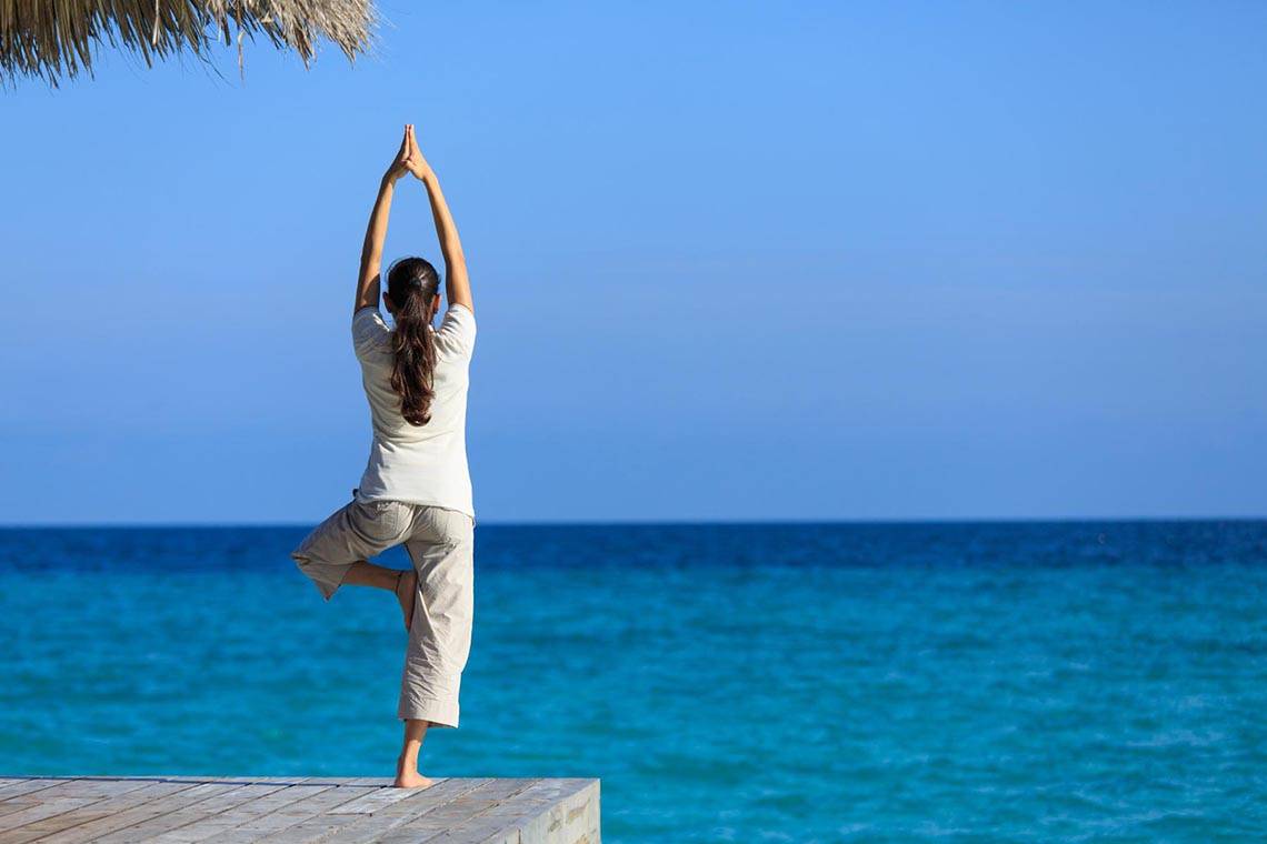 Eine Frau praktiziert Yoga auf einem Steg am Strand des Kuramathi Maldives Hotels.