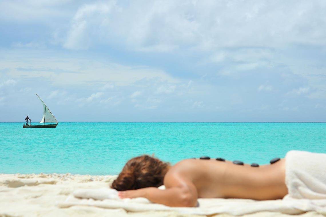 Eine Person genießt eine Massage auf dem Strand von Kuramathi Maldives mit einem Boot im Hintergrund.