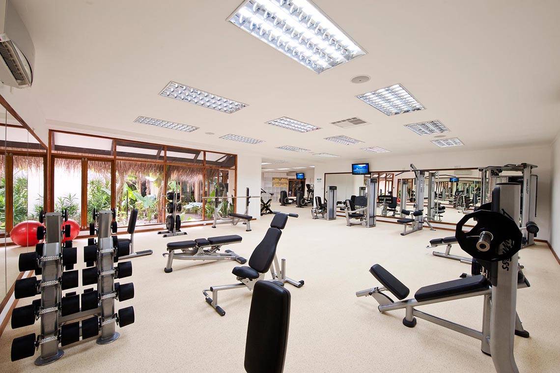Fitnesscenter im Kuramathi Maldives Hotel mit vielen Geräten und großen Fenstern.