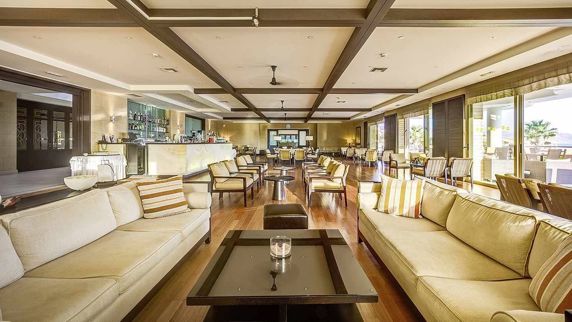Loungebereich des Candia Maris Resort & Spa mit gepolsterten Sofas, Tischen und einer Bar.