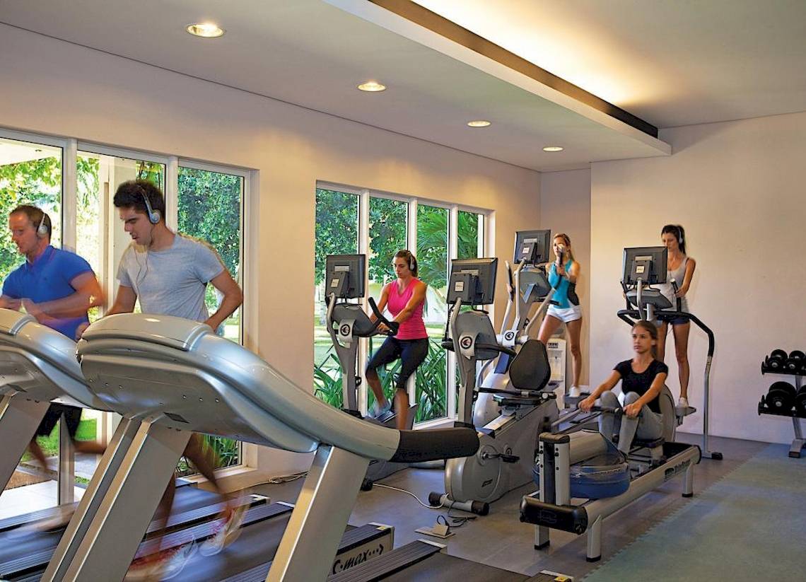 Fitnessraum im La Pirogue Mauritius Hotel mit mehreren Personen, die auf verschiedenen Trainingsgeräten trainieren.