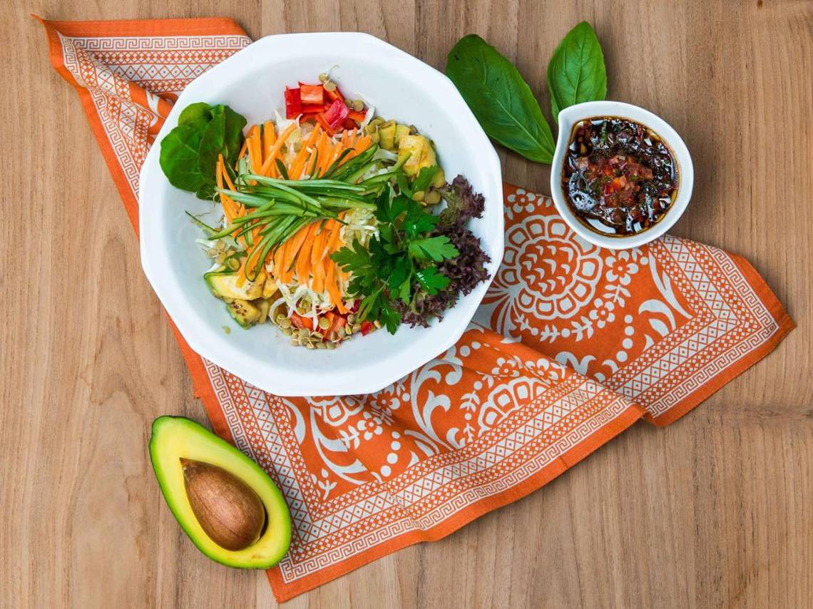 Teller mit Gemüsesalat und Avocado auf einem orangefarbenen Tuch