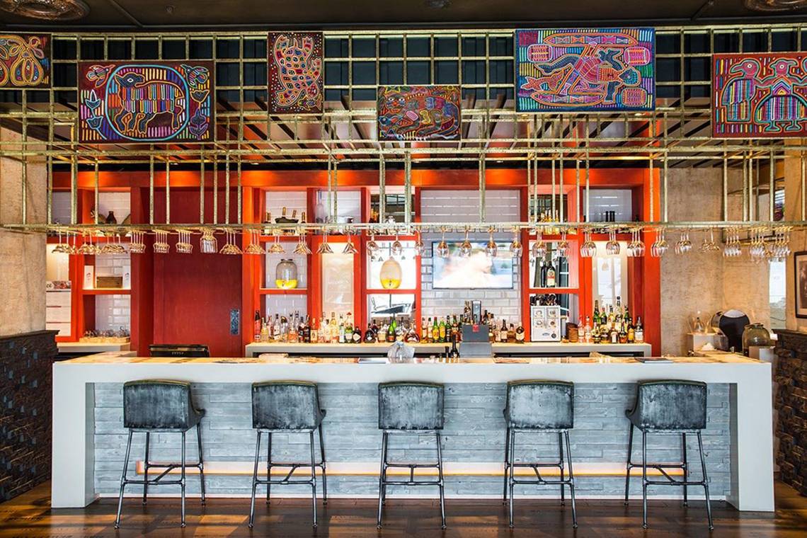 Innenansicht der Bar im Akra Hotel mit goldenen Metallrahmen, dekorativen Wandmalereien und grauen Barhockern.