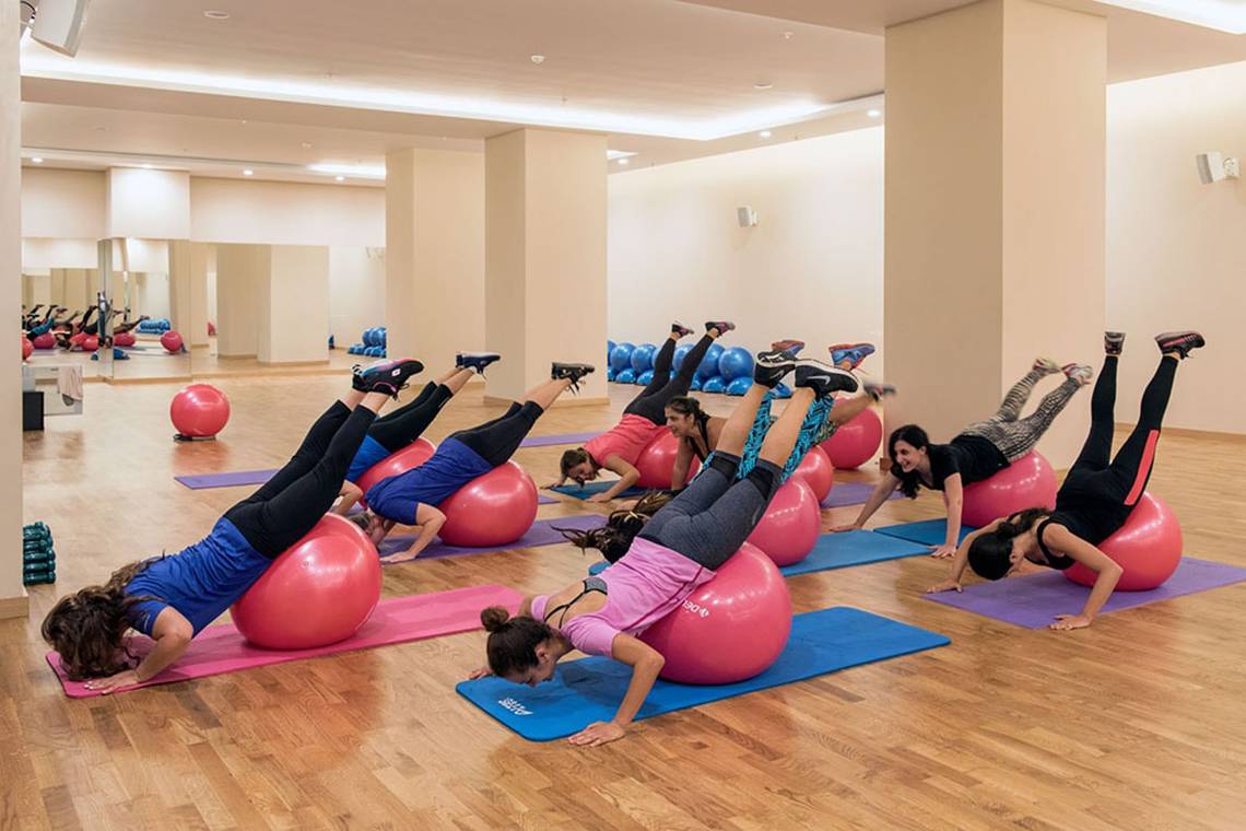Gruppe von Frauen im Akra Hotel Fitnessraum, die einen Aerobic-Kurs absolvieren und auf roten Fitnessbällen balancieren.