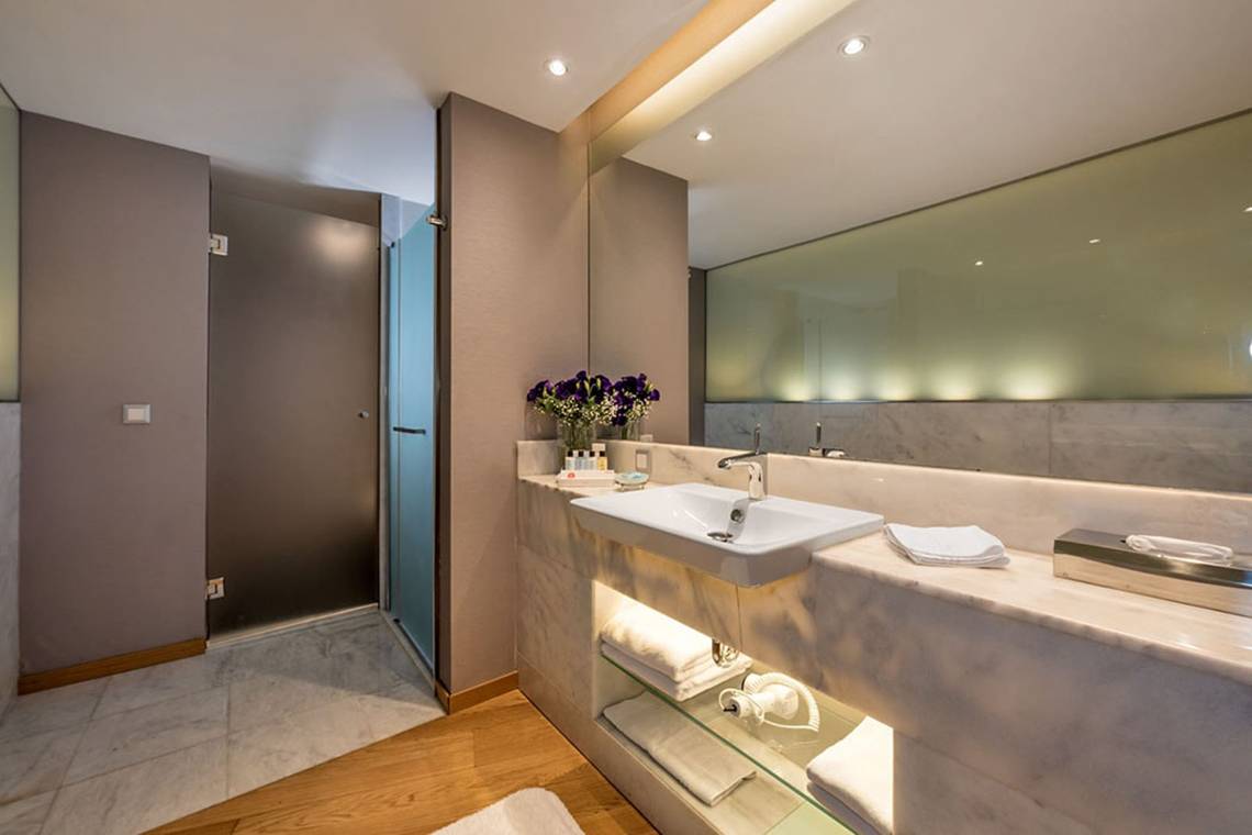 Badezimmer im Akra Hotel mit großem Spiegel und Blumen auf dem Waschtisch.