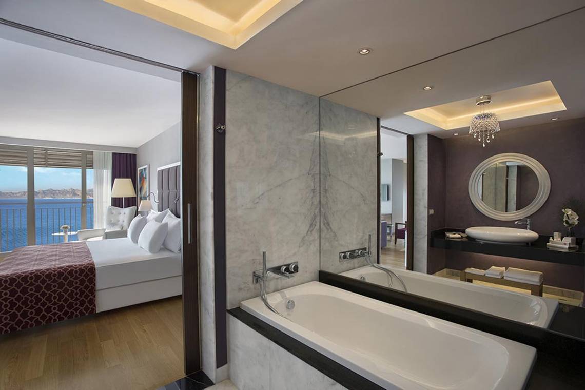 Schlafzimmer des Akra Hotels mit Blick auf das Meer und einem großen Bett, umgeben von weißen Kissen.