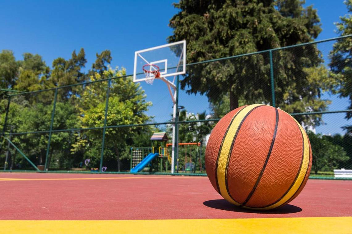 Ein Basketball liegt auf einem Spielplatz, mit einem Basketballkorb im Hintergrund.