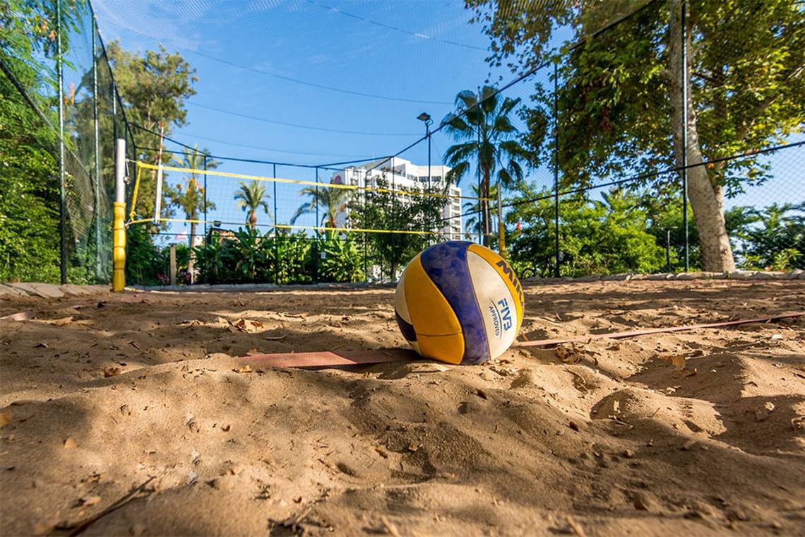 Ein Volleyball liegt auf einem Sandplatz vor einem Hotel.