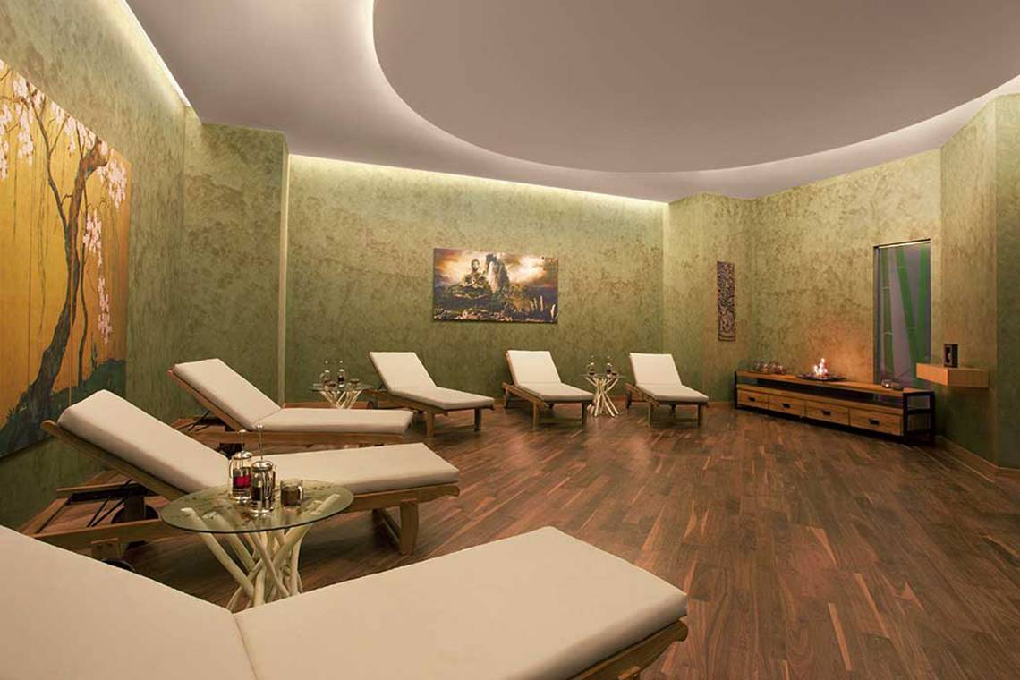 Spa-Lounge im Akra Hotel mit mehreren weißen Liegen, Holzboden und grünen Wänden.
