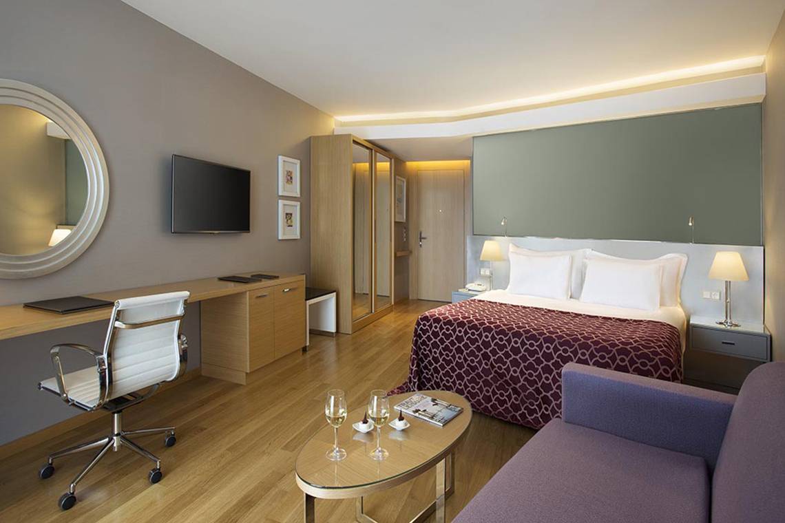 Innenansicht eines Zimmers im Akra Hotel mit Bett, Schreibtisch, Stuhl und Couch.
