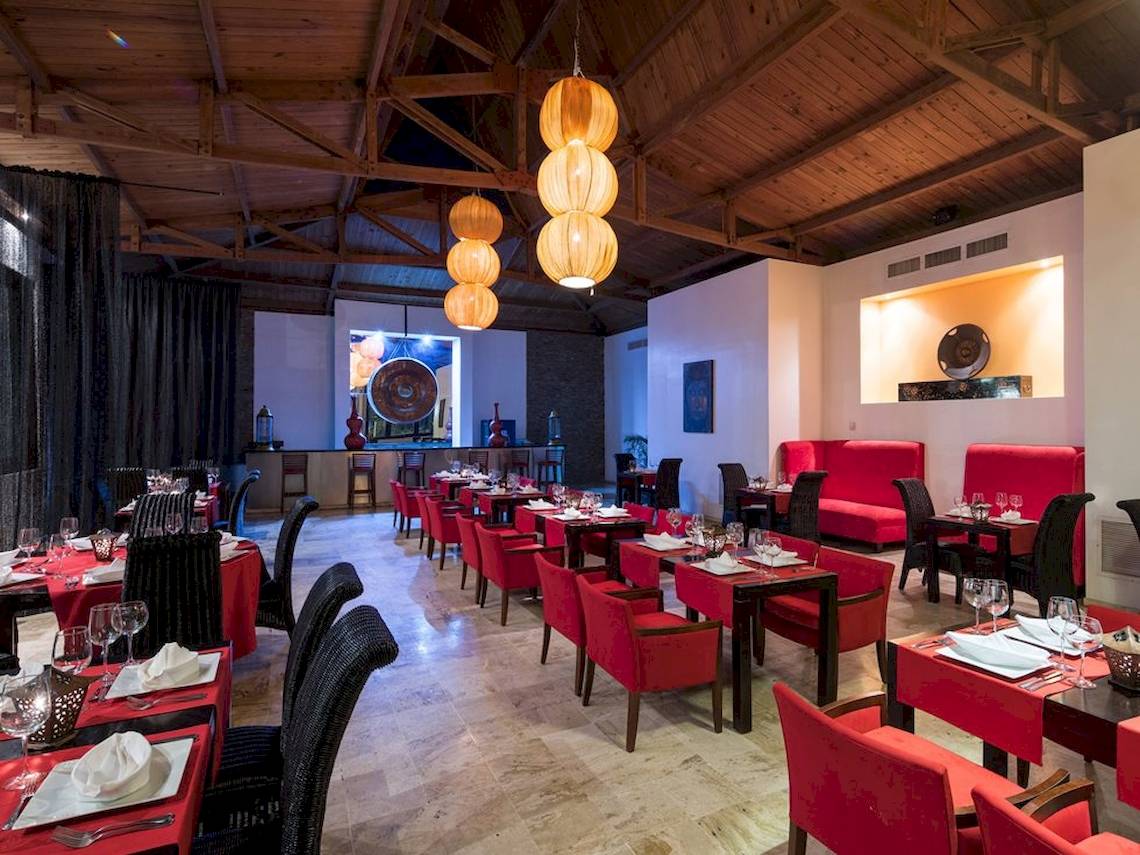 Innenbereich des BlueBay Villas Doradas Restaurants mit roten Stühlen, Tischen und dekorativen Lampen.