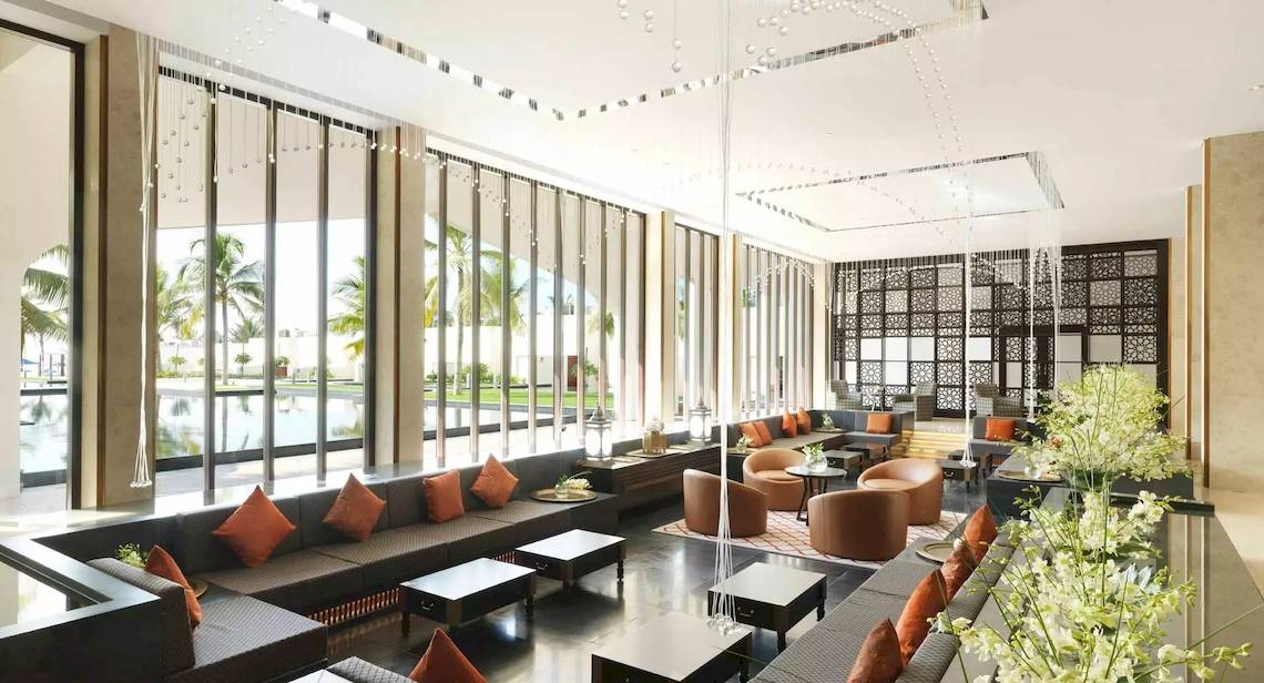 Lobby des Al Baleed Resort Salalah von Anantara mit großen Fenstern und modernen Möbeln.