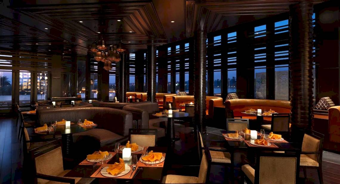 Innenansicht des Al Baleed Resort Salalah by Anantara Restaurants mit runden Tischen und Kerzen.