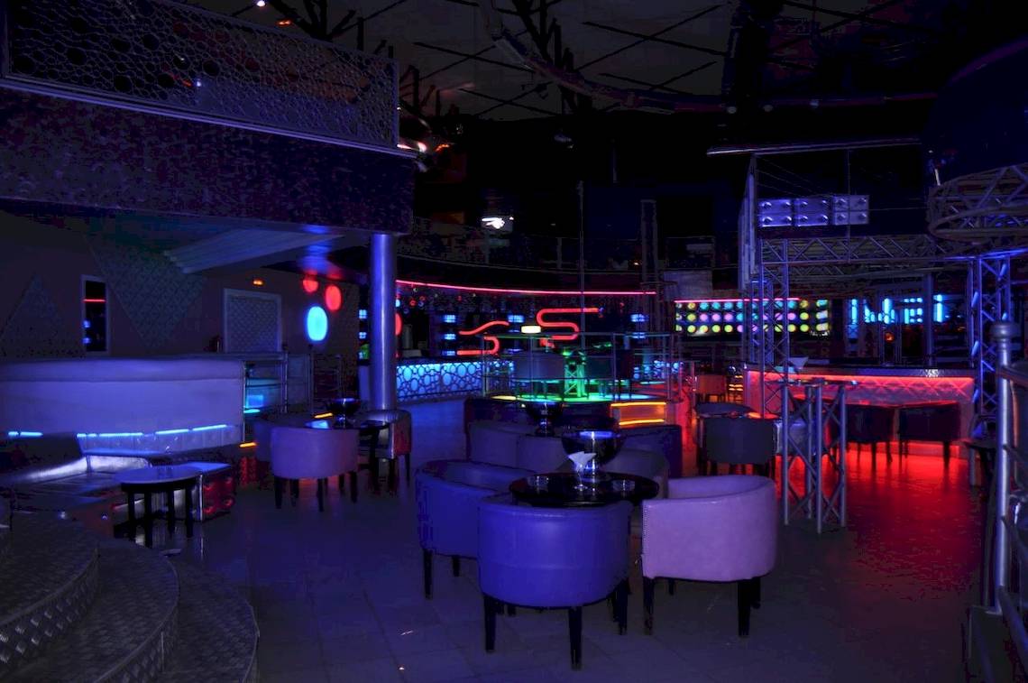 Innenbereich des Green Palm Hotels mit blauen und roten Neonlicht-Dekorationen, Tischen und Stühlen.