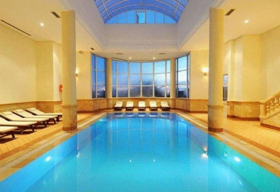 Indoorpool des Green Palm Hotels mit blauem Wasser und Sonnenliegen.