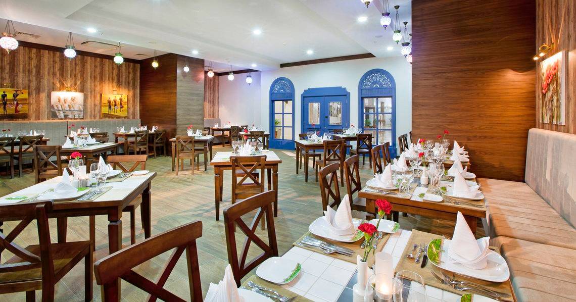 Innenansicht des Restaurants des Adalya Ocean Deluxe Hotels mit gedeckten Tischen und dekorierten Wänden.