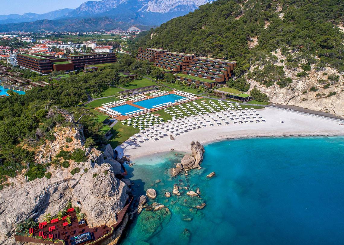 Luftaufnahme des Maxx Royal Kemer Resort mit Swimmingpool, weißen Liegen und türkisfarbenem Meer