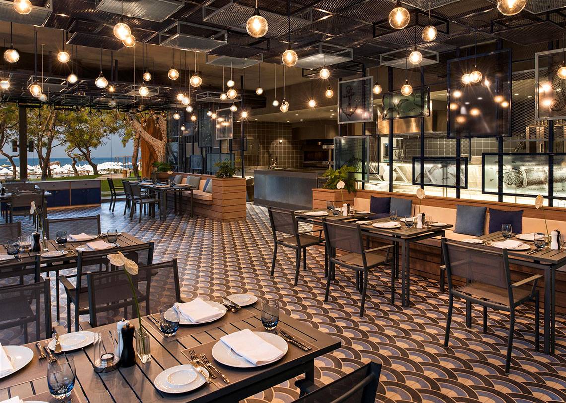 Innenansicht des Restaurants im Maxx Royal Kemer Resort mit geometrischem Bodenmuster und hängenden Lampen.