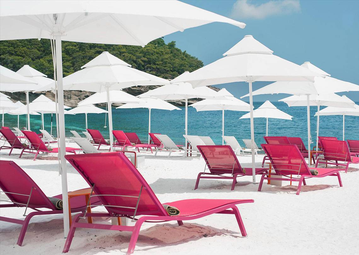 Strand des Maxx Royal Kemer Resorts mit roten Liegestühlen und weißen Sonnenschirmen.