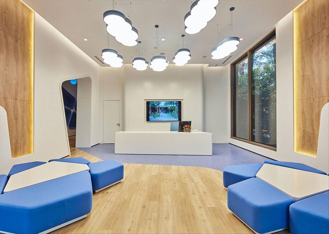 Lobby des Maxx Royal Kemer Resort mit blauen Sitzmöbeln, weißem Schreibtisch und Fernseher.