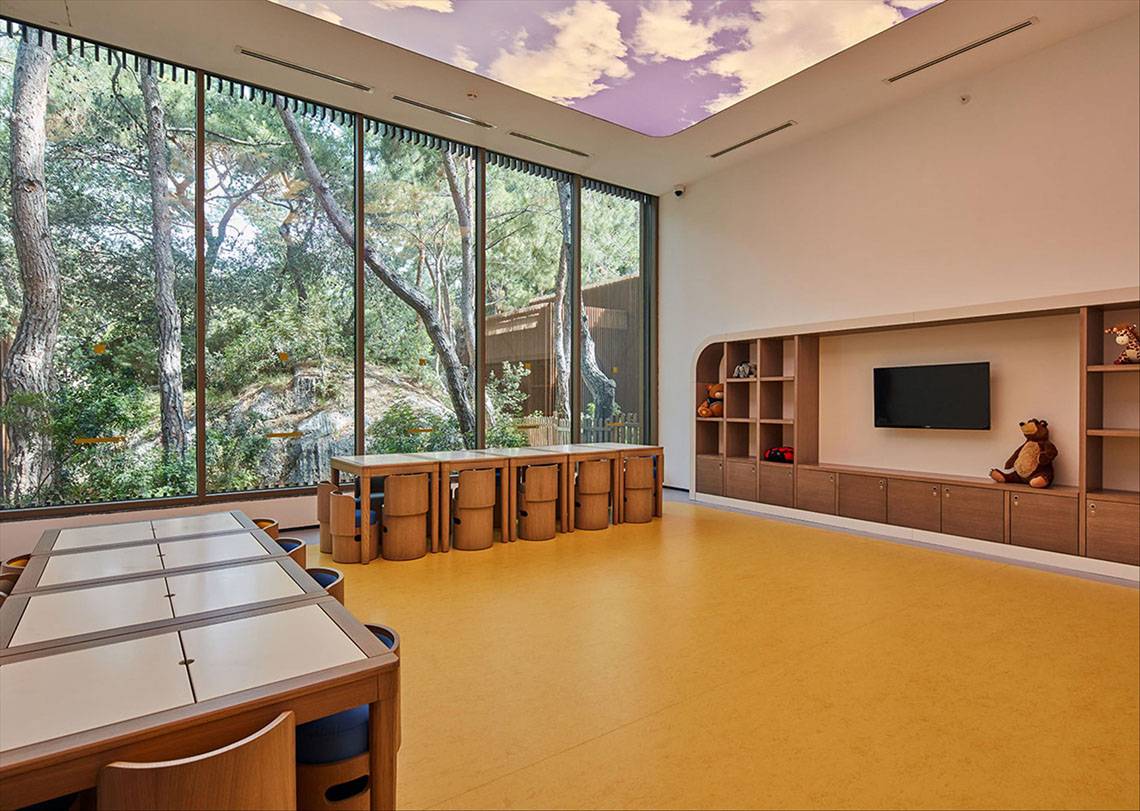 Ein Kinderzimmer im Maxx Royal Kemer Resort mit großen Fenstern und Panoramaaussicht auf einen Wald.